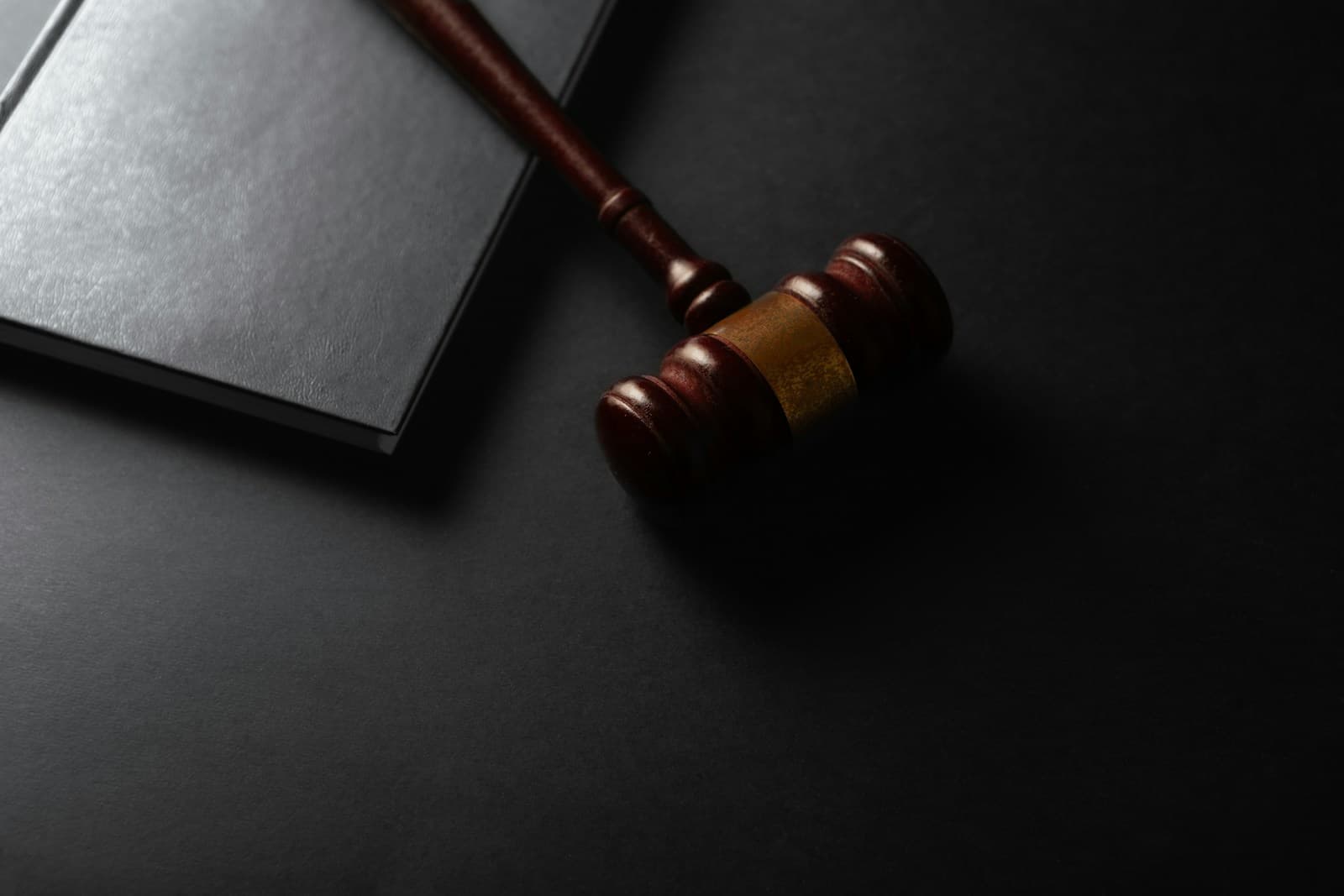 Wooden gavel resting on a dark surface next to a law book